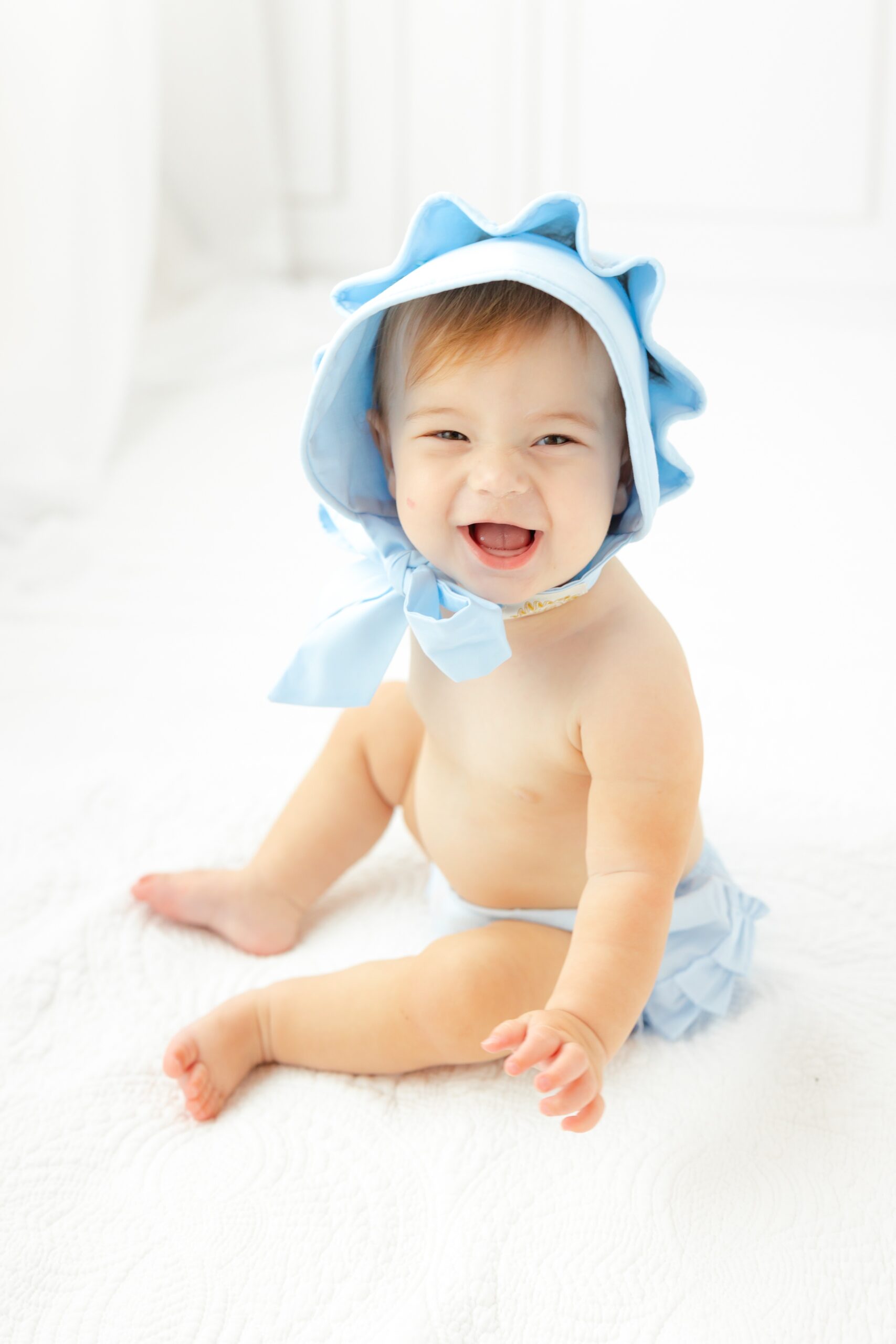 A happy baby sits in a blue bonnet and matching underwear in a studio on a bed before some things to do with kids in savannah