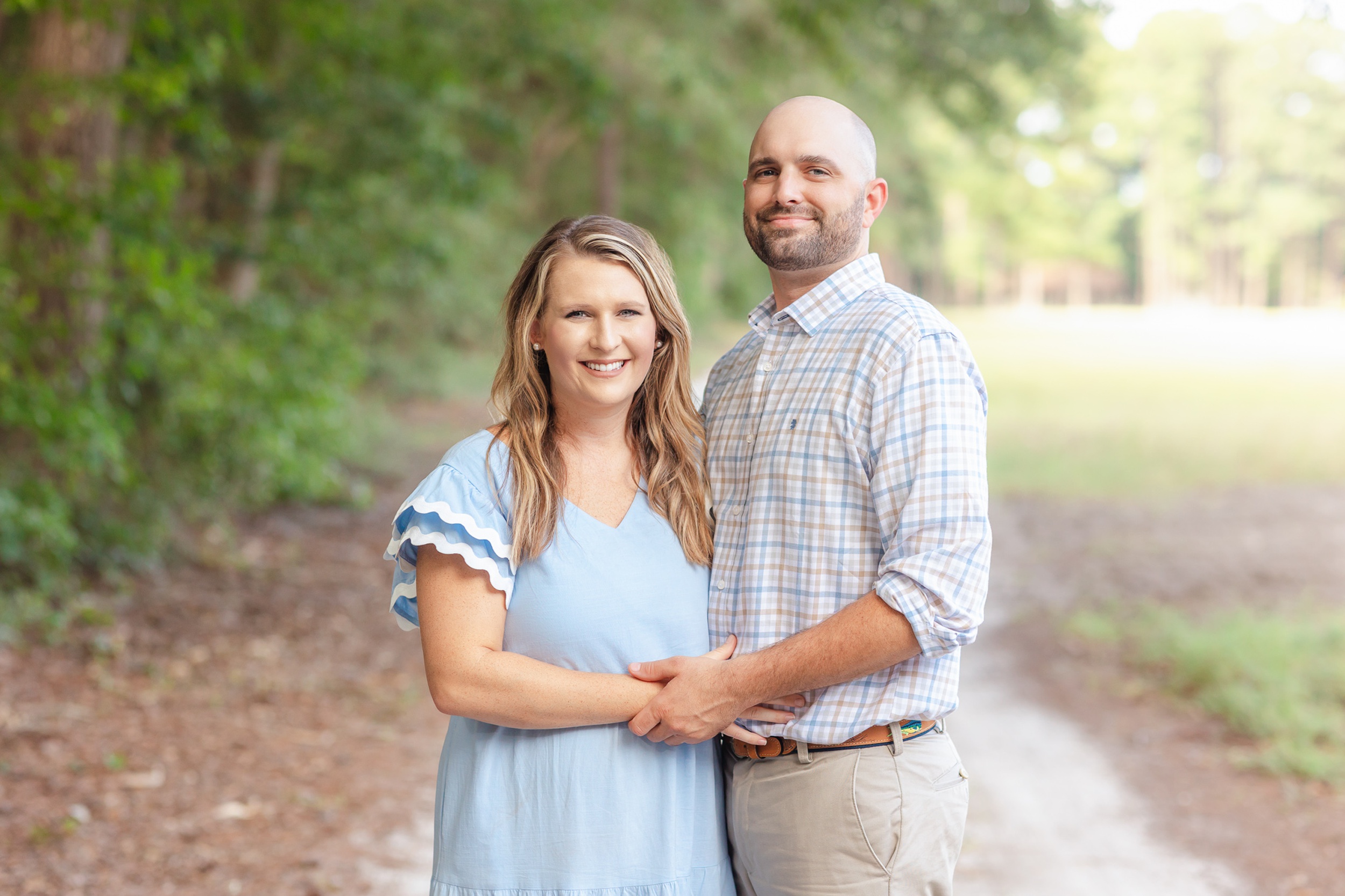 Happy parents stand together in a park trail holding hands in blue and tan