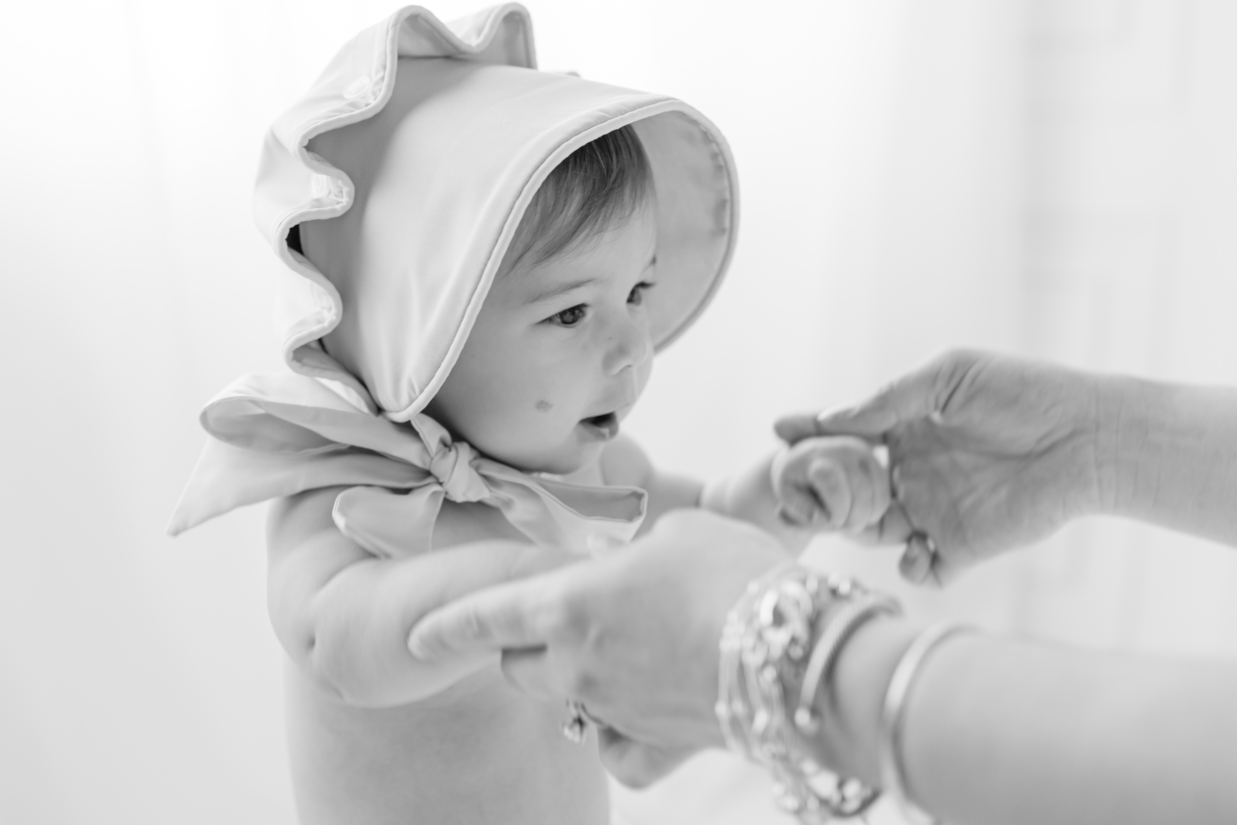 A baby in a bonnet walks with mom's help in black and white before some birthday parties in savannah ga