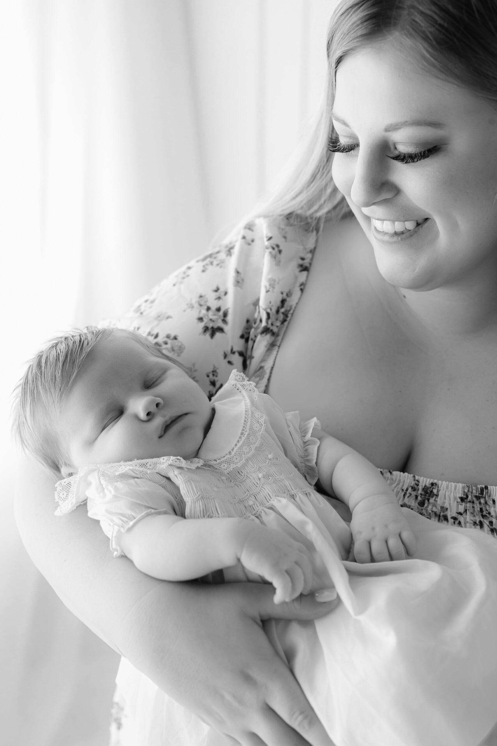 A happy mom smiles while holding her sleeping baby in a studio