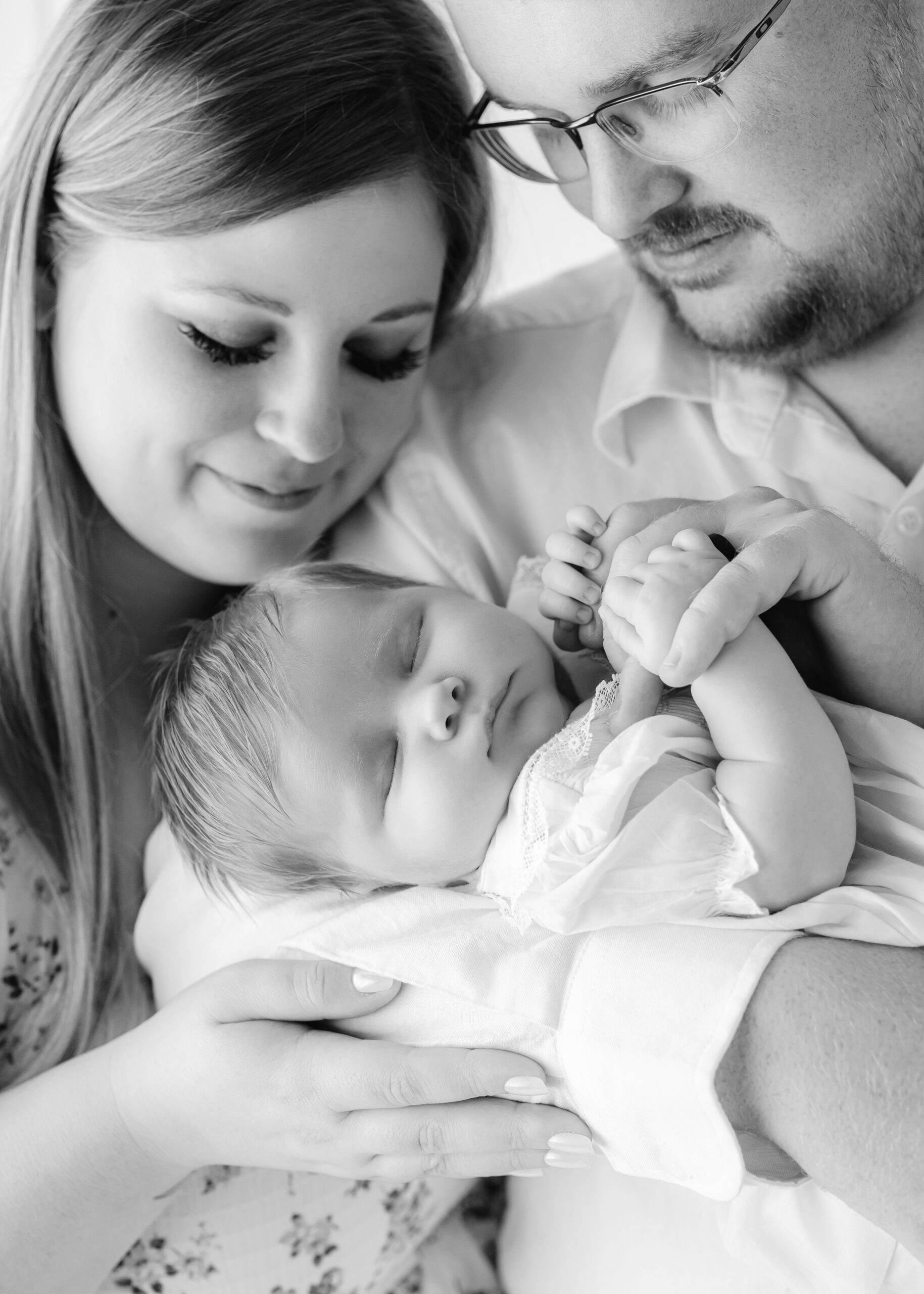 A newborn holds dad's fingers while sleeping in his arms with mom smiling before visiting family friendly restaurants in Savannah