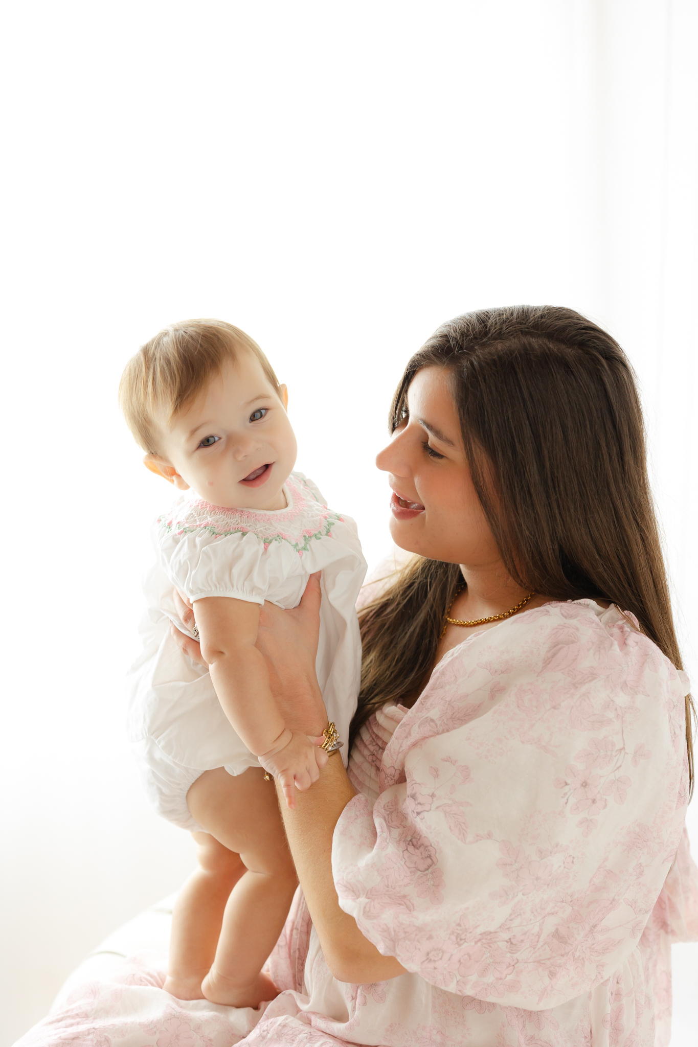 mom wearing a pink designer dress looking at her 9 month old and smiling. 9 month old girl is smiling at the camera. mommy and me classes savannah ga