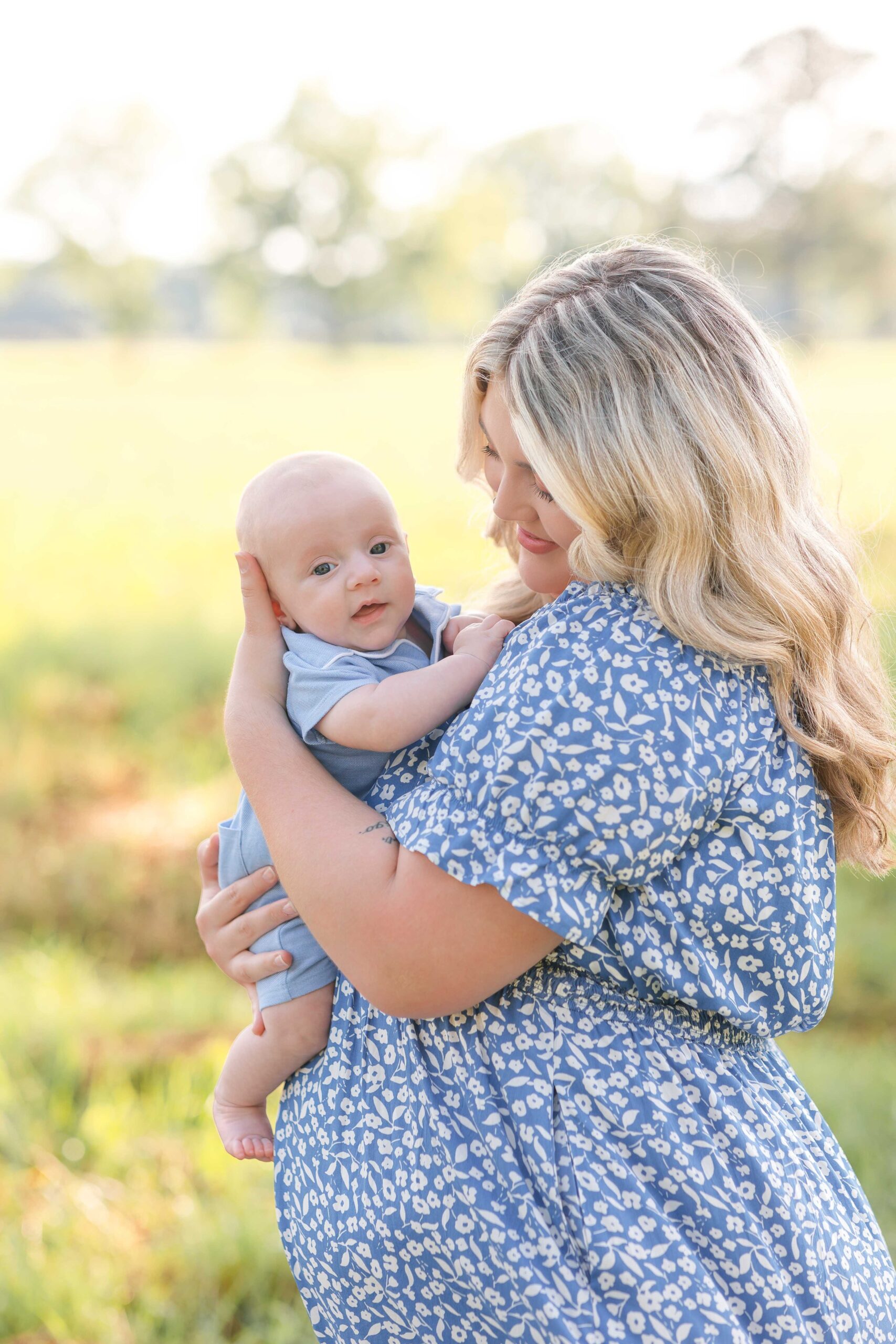 A new mom in a blue floral dress holds her baby against her chest in a park