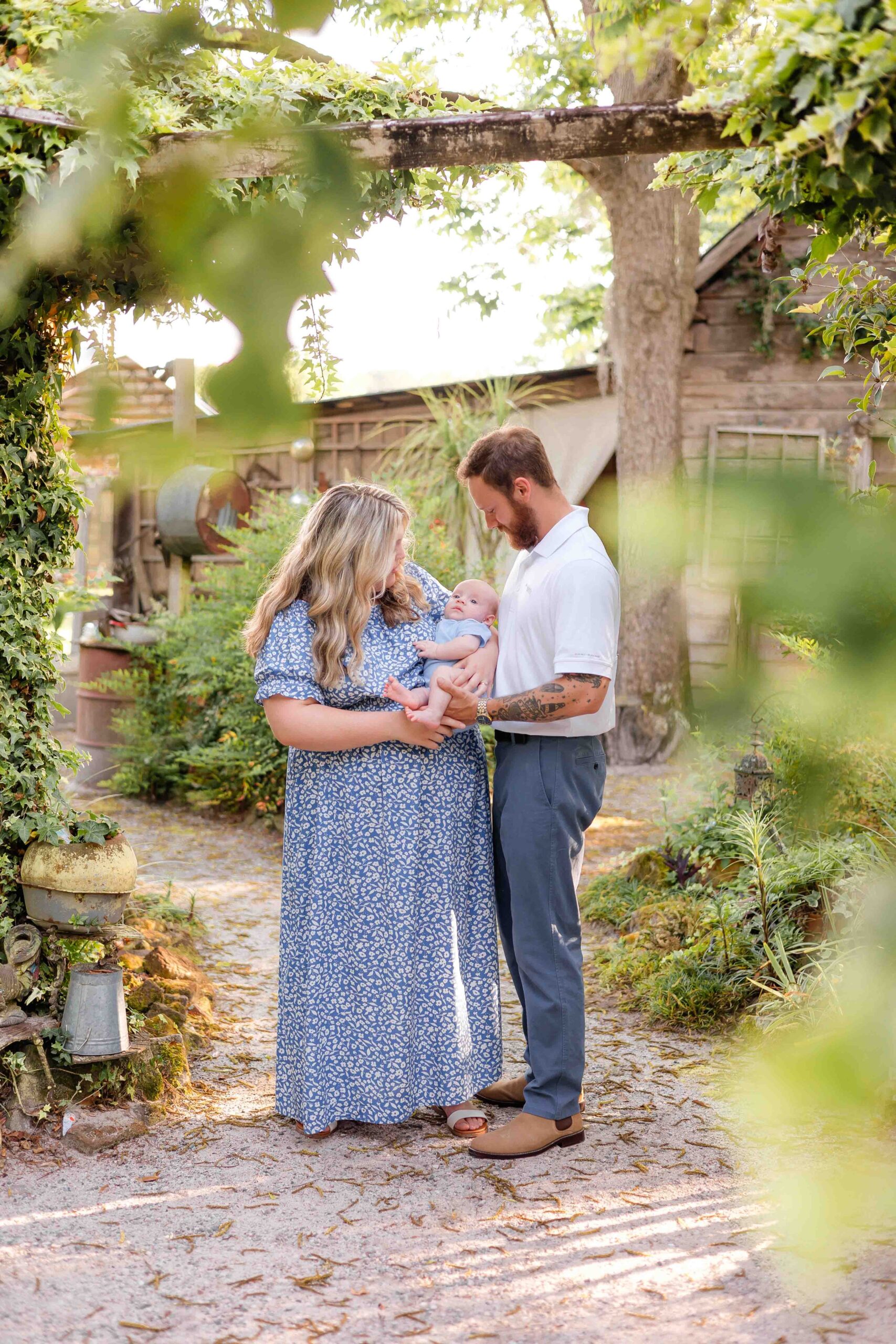 Happy new parents stand in a garden with their newborn in blue while exploring parks in savannah