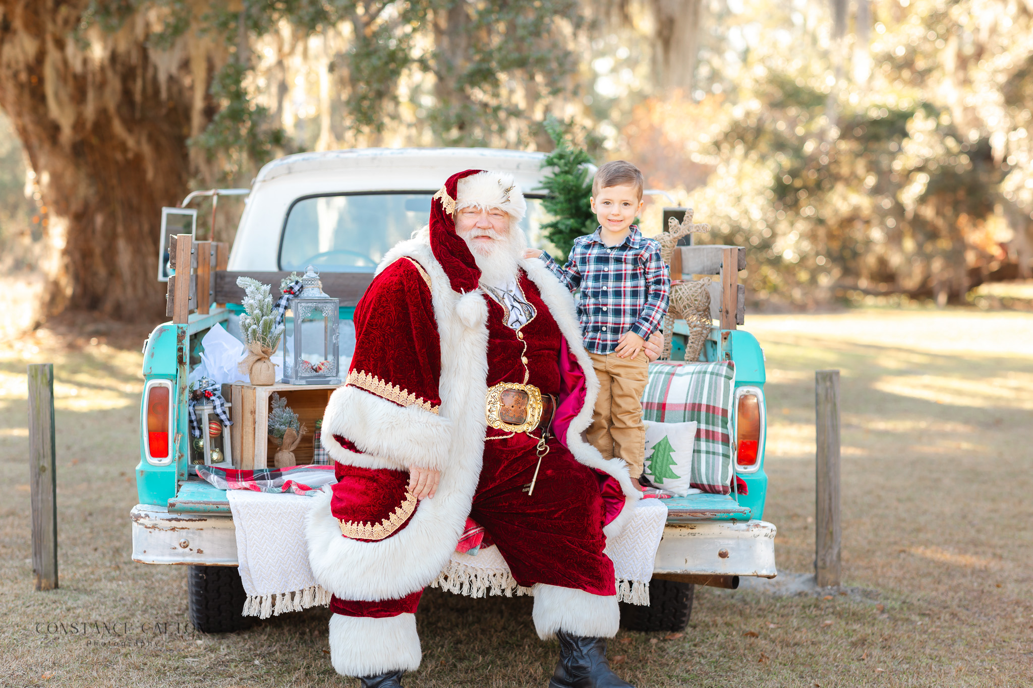 Toddler sitting with Santa by a vintage blue truck during Savannah Santa Pictures session
