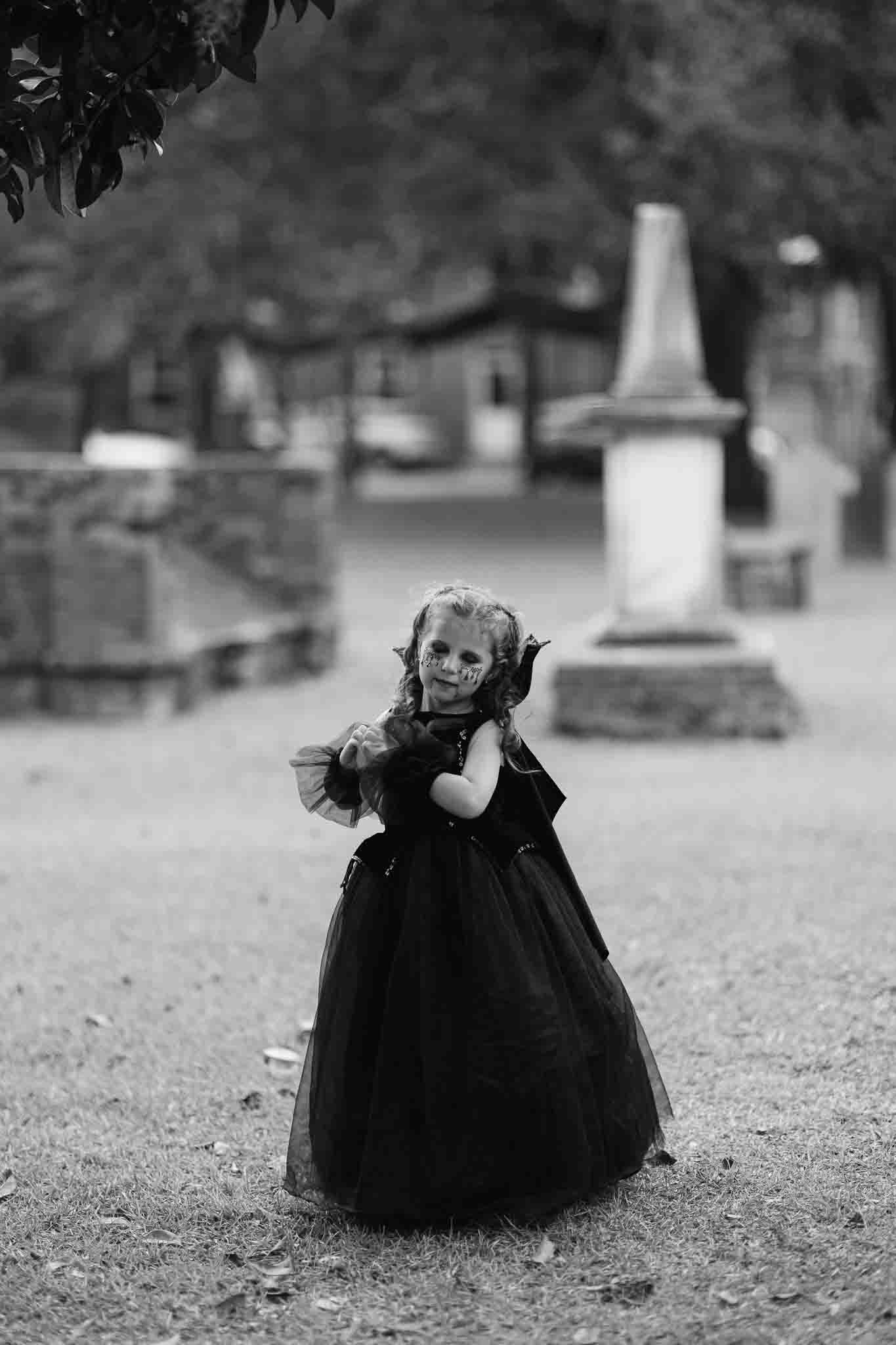 Little girl wearing a vampire costume posing in the colonial cemetery in Savannah, ga by a crypt 