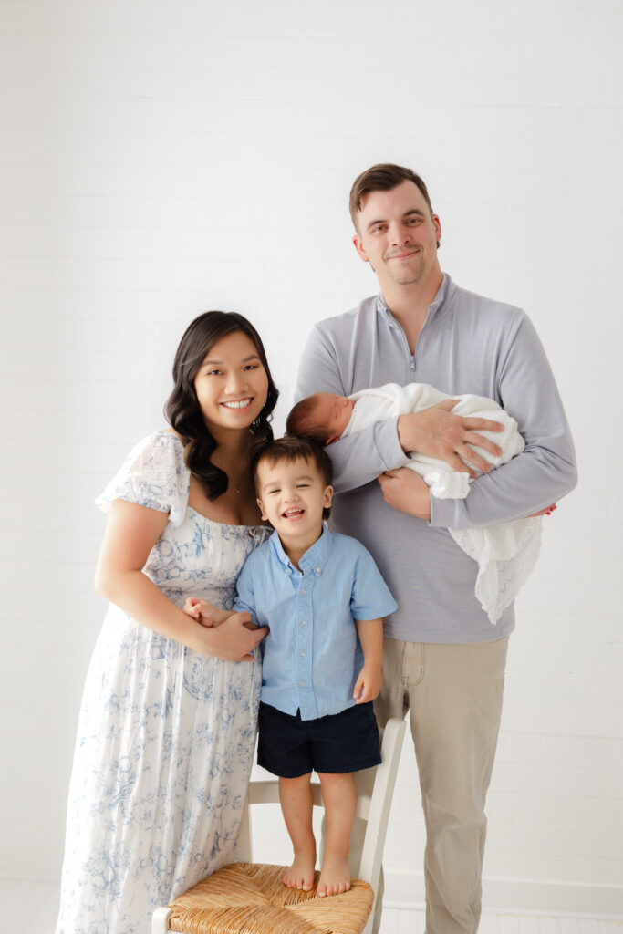 Family of 4 smiling at the camera with their newborn baby boy and big brother