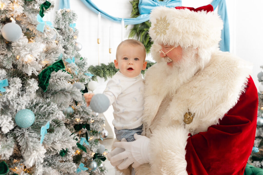 Santa holding little boy who is playing with some Christmas ornaments on the tree. Studio in Savannah, GA