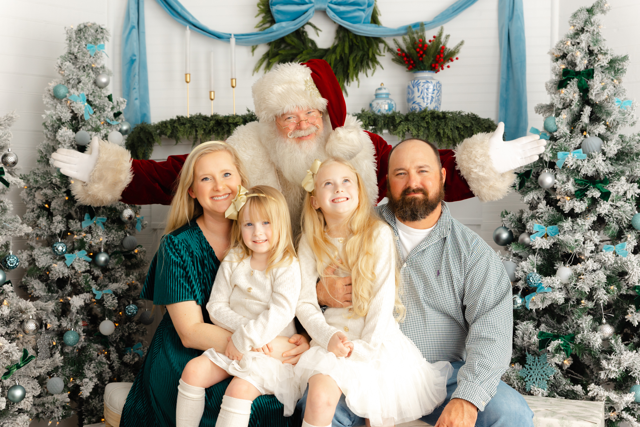 Family of 4 with 2 girls posing with Santa in a studio for Christmas pictures