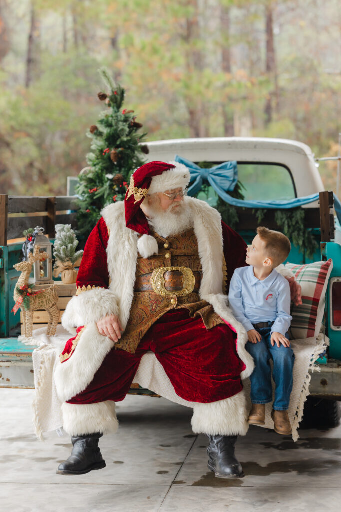 Santa talking with a young boy during an outdoor santa photoshoot with blue truck photography experience.