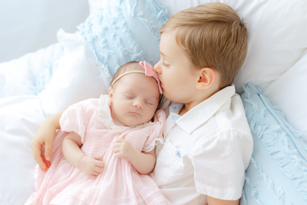 Three year old big brother kissing his newborn baby sister during newborn photos with a toddler sibling.