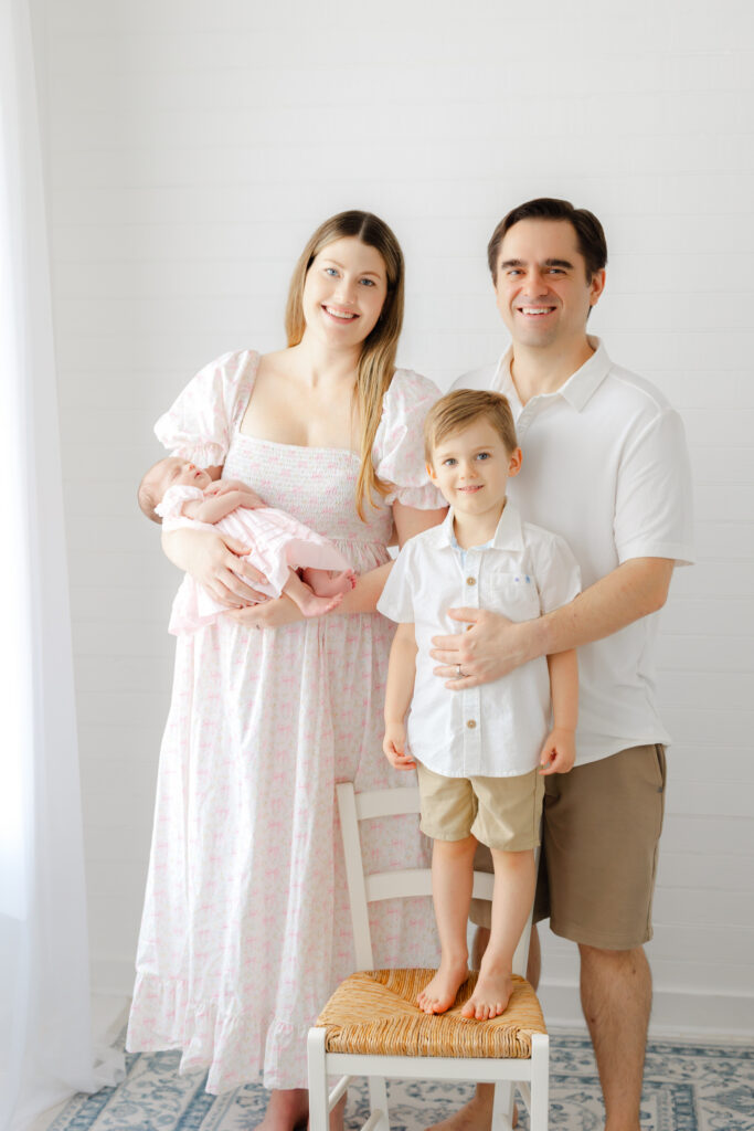 Family wearing coordinated soft neutral and pastel outfits for newborn photos in a light Savannah photography studio.