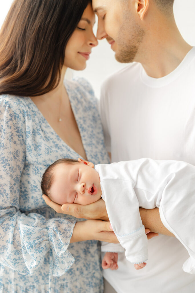 Mom and Dad cuddling their newborn while wearing soft coordinating colors for their newborn family photos.