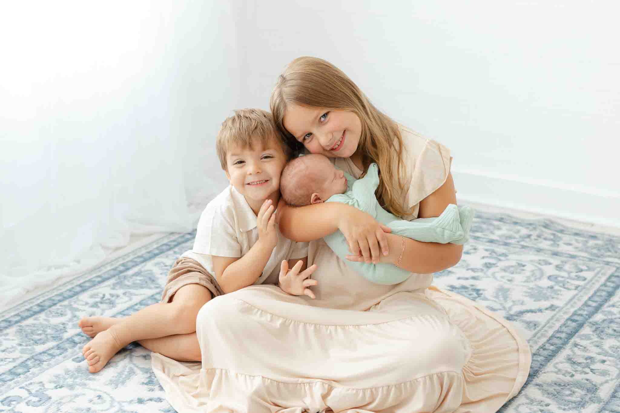 Newborn baby and older brother and sister wearing coordinating cream and beige sibling outfits for newborn photos.