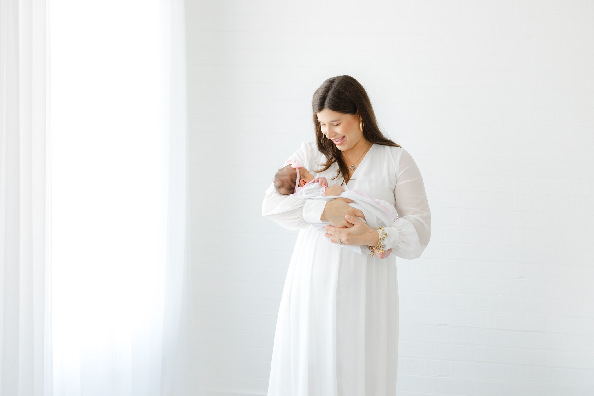 Mom wearing a flowing white dress while holding her newborn baby during a studio newborn photography session.